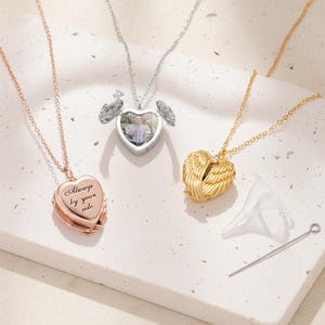 May include: Three heart-shaped locket necklaces in rose gold, silver, and gold. The rose gold locket has the inscription "Always by your side." The silver locket opens to reveal a photo. The gold locket has wing details and a small funnel and pin.