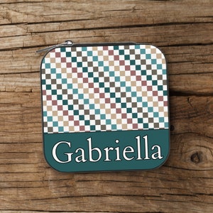 May include: A teal zippered pouch with a checkered pattern in shades of brown, beige, and blue. The pouch has the name "Gabriella" printed in white on the front.