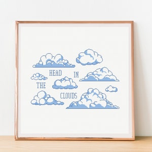 May include: A framed print with a white background and blue pixelated clouds. The text "HEAD IN THE CLOUDS" is written in blue.