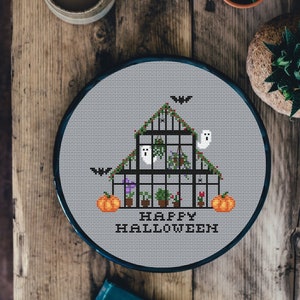 May include: Cross stitch pattern of a spooky greenhouse with ghosts, bats, and pumpkins. The text "Happy Halloween" is stitched below the greenhouse.