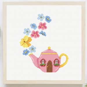 May include: Cross-stitch artwork in a light wooden frame. The image features a pink teapot with a yellow handle and spout, and a brown door. Colorful flowers in yellow, pink, and blue appear to be flowing from the spout.