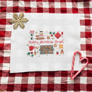 May include: White cross-stitch embroidery with a Christmas baking theme. The embroidery features a variety of festive baking items, including a gingerbread house, cookies, and a rolling pin. The text "Baking Christmas Bright" is stitched in red thread.