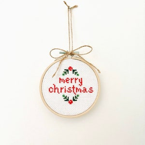 May include: A white embroidery hoop with a red "Merry Christmas" message and green holly leaves with red berries.