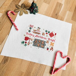 May include: White cross-stitch embroidery with a Christmas baking theme. The design features a gingerbread house, cookies, and the text "Baking Christmas Bright".