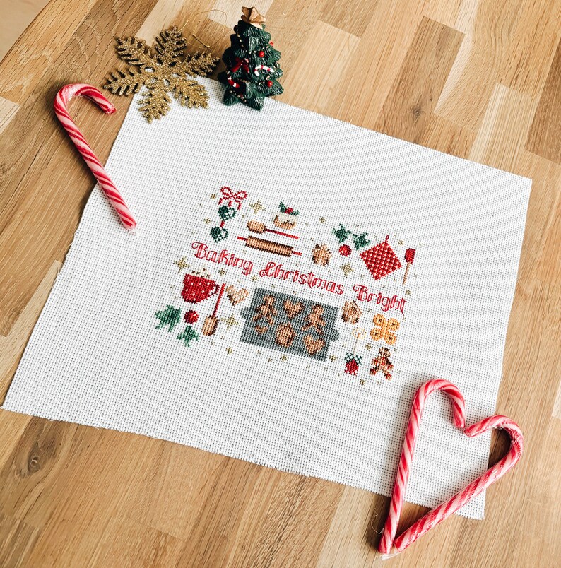 May include: White cross-stitch embroidery with a Christmas baking theme. The design features a gingerbread house, cookies, and the text "Baking Christmas Bright".