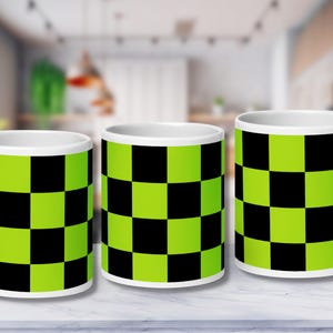 Könnte beinhalten: Drei weiße Keramikbecher mit einem schwarz-grünen Karomuster. Die Becher sind in einer Reihe auf einer weißen Oberfläche angeordnet.
