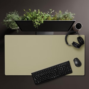 May include: Overhead view of a modern desk setup with a beige desk mat. A black computer monitor sits atop the desk, with greenery in a trough above it. A black keyboard, mouse, and headphones are also on the desk, along with a coffee cup.