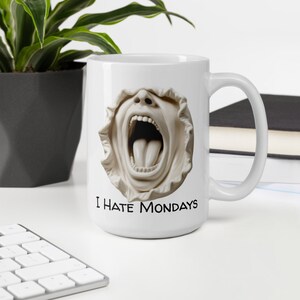 Könnte beinhalten: Weiße Keramik-Kaffeetasse mit einem Grafikdruck eines schreienden Gesichts und dem Text "I Hate Mondays".