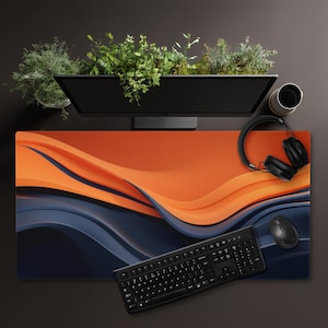 May include: A large desk mat featuring an abstract design in orange and navy blue. A black keyboard, mouse, and headphones are on the mat. A computer monitor and a cup are in the background.