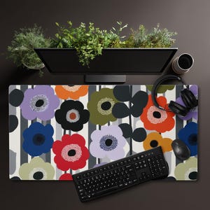 May include: A floral patterned desk mat featuring large, colorful flowers in shades of purple, orange, red, blue, and green against a gray and white striped background. A black keyboard, mouse, and headphones are on the mat.