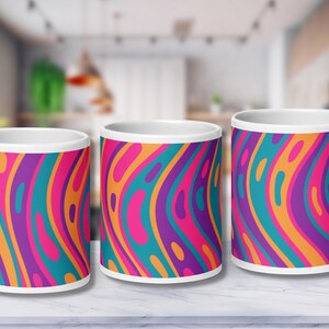Könnte beinhalten: Drei weiße Keramikbecher mit einem farbenfrohen abstrakten Design. Das Design zeigt wellenförmige Linien in den Farben Pink, Lila, Orange und Türkis.