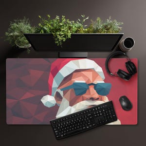May include: A rectangular desk mat featuring a low-poly geometric illustration of Santa Claus wearing blue sunglasses and a red hat. The design uses shades of red, white, and blue in a faceted pattern. A black keyboard, mouse, and headphones sit on top.