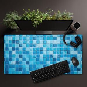 Peut inclure: Un bureau avec un tapis de souris à motif de carreaux bleus, un clavier noir, une souris et un casque. Un écran d'ordinateur avec de la verdure au-dessus est en arrière-plan. Une tasse et un petit pot de plantes sont également visibles.