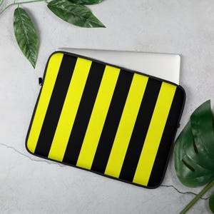 Könnte beinhalten: Schwarze und gelbe gestreifte Laptoptasche. Die Tasche ist aus weichem, strapazierfähigem Material gefertigt und verfügt über einen Reißverschluss.