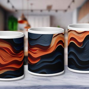 May include: Three white ceramic mugs with a wraparound abstract design. The design features flowing, layered patterns in shades of orange, navy blue, and black. The mugs are displayed on a marble surface.