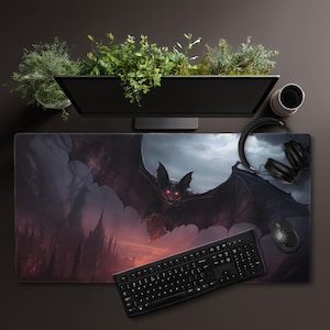 May include: A large rectangular mousepad featuring a dark fantasy illustration of a bat with glowing red eyes against a stormy sky. A black keyboard, mouse, and headphones are also visible.