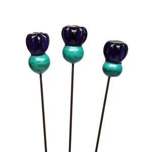 May include: Three decorative glass flower picks. Each pick has a dark blue, textured top and a turquoise, spherical base. The picks are mounted on thin, dark brown metal stems, creating a whimsical floral accent for home decor or crafts.