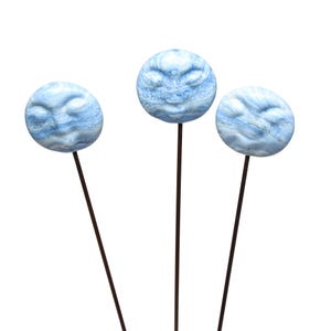 Peut inclure: Trois piquets de jardin décoratifs avec des sphères rondes bleu et blanc marbré, ornées d'un visage. Les sphères sont fixées sur de fines tiges métalliques marron foncé, créant un accent artistique pour le jardin.