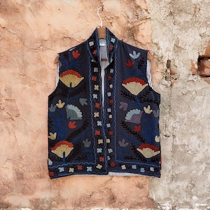 May include: A black sleeveless vest with a floral embroidery pattern in shades of blue, red, and yellow. The vest has a collar and a button closure.
