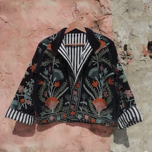 May include: A black velvet jacket with a floral embroidery design. The jacket has a striped lining and a collar.