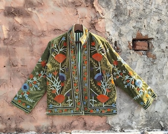 May include: Olive green jacket with floral embroidery in orange, blue, and white. The jacket has a mandarin collar and a striped green and white lining. The embroidery features stylized flowers and leaves. The jacket is hanging on a wooden hanger.
