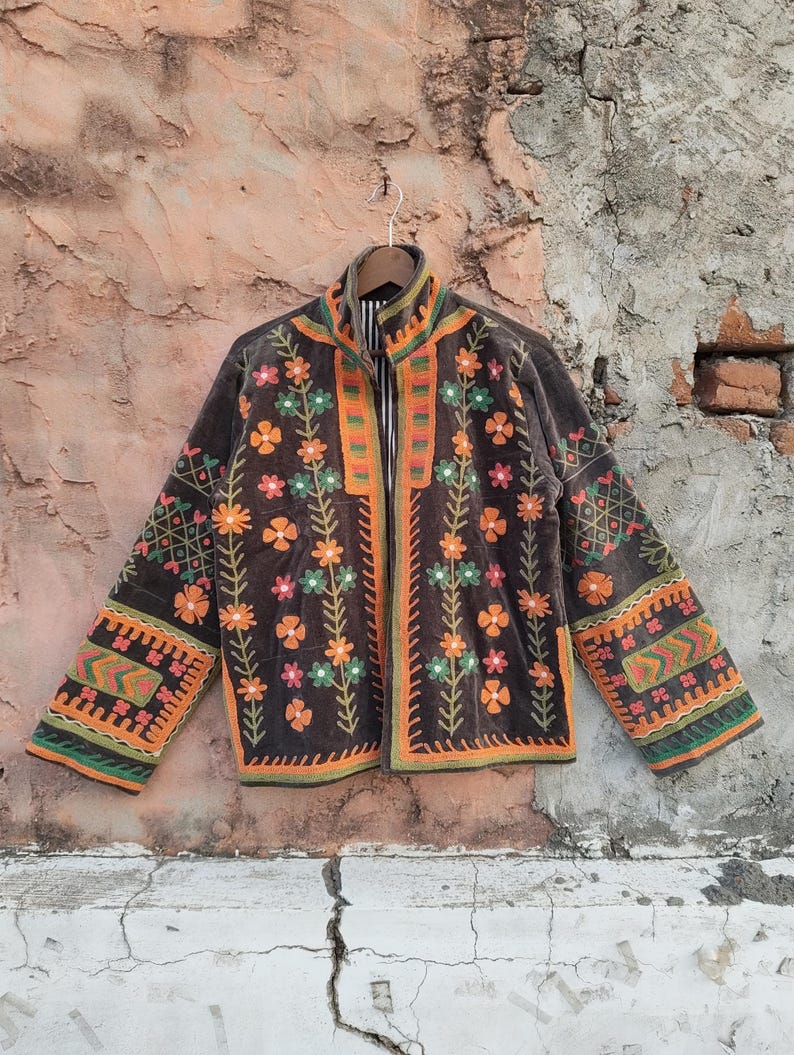 May include: A brown embroidered jacket with floral and geometric patterns in orange, green, and pink. The jacket has a high collar and long sleeves. The embroidery is detailed and covers the front, sleeves, and collar.