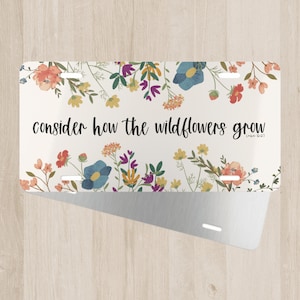 May include: A white metal license plate with a floral design and the text "consider how the wildflowers grow" with the scripture reference "Luke 12:27".