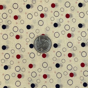May include: Cream-colored fabric with a repeating pattern of red and navy blue dots and black outlined circles. A quarter coin is placed on the fabric for scale. The fabric has a vintage or retro aesthetic.