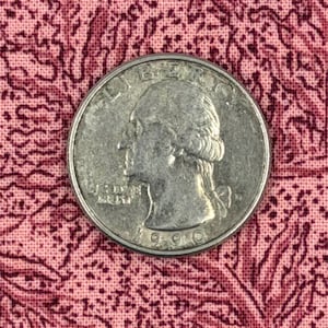 May include: A silver-colored United States quarter dollar coin featuring the profile of George Washington facing left. The coin is inscribed with the word LIBERTY at the top, the phrase IN GOD WE TRUST on the left, and the year 1990 at the bottom.
