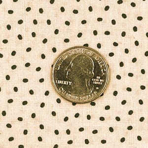 May include: Close-up of a beige fabric with a repeating pattern of dark green polka dots. A United States quarter coin is centered on the fabric, providing a size reference. The fabric has a textured appearance.