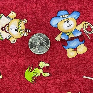 May include: Red fabric with a repeating pattern of cartoon teddy bears dressed as cowboys and Native Americans. The bears are in various poses, with a quarter coin for scale. The fabric has a textured appearance.