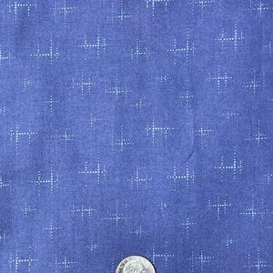 May include: A close-up of a blue fabric with a white dotted pattern. The pattern is made up of small white dots arranged in the shape of a cross. A US quarter is included for scale.