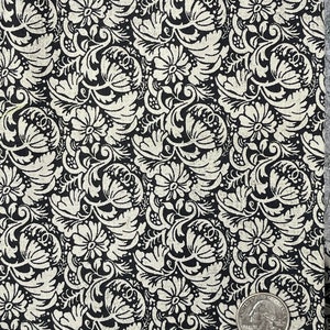 以下が含まれることがあります： 白い花の模様が施された黒い布。模様は複雑な渦巻きと葉で構成されています。スケールのために、アメリカの25セント硬貨が付属しています。