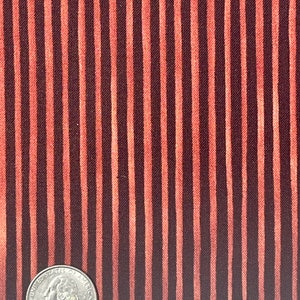 以下が含まれることがあります： 茶色とオレンジの縦縞模様の生地のクローズアップ。生地の上にアメリカの25セント硬貨が置かれており、スケールを示しています。