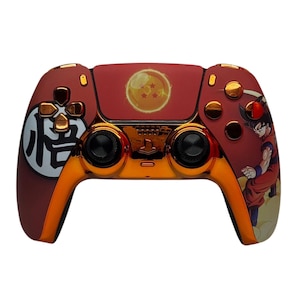 May include: A gold and red PlayStation 5 controller with a Dragon Ball Z themed design. The controller features a red background with a gold trim, a Dragon Ball Z character on the right side, and a Dragon Ball Z symbol on the left side.