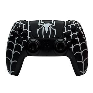 May include: A black PlayStation 5 controller with a white spider web design and a white spider graphic on the top.