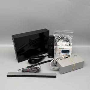Könnte beinhalten: Eine schwarze Wii-Konsole mit Fernbedienung, Sensorleiste und Netzteil. Das Bild enthält auch eine Wii-Fernbedienung und einen Wii-zu-HDMI-Konverter.
