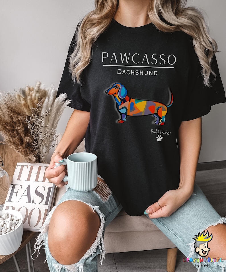 May include: Black t-shirt with a white graphic of a colorful dachshund with the text "PAWCASSO" and "DACHSHUND" above the dog and "Pawcasso" below the dog.