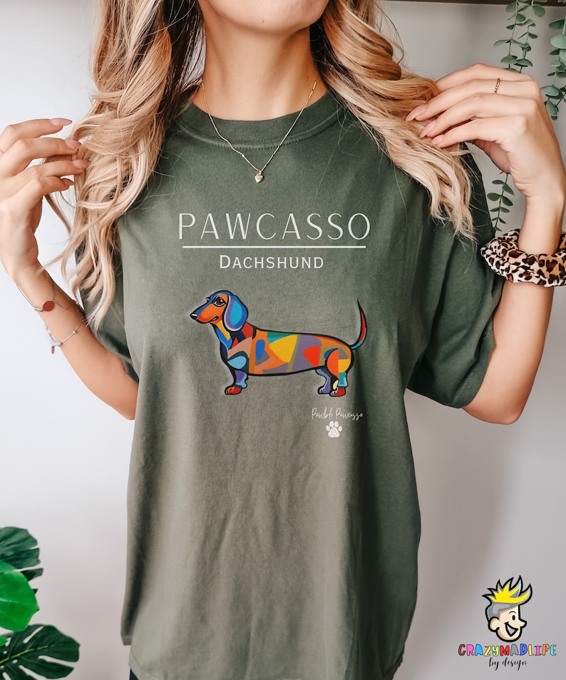 May include: Green t-shirt with a colorful dachshund illustration and the text "PAWCASSO Dachshund" printed on the front. The dachshund is in a colorful abstract style with the text "Pawcasso" below it.