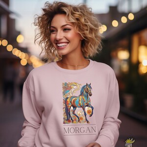 以下が含まれることがあります： カラフルな馬のデザインと「MORGAN」という名前が下に印刷されたピンク色のスウェットシャツです。