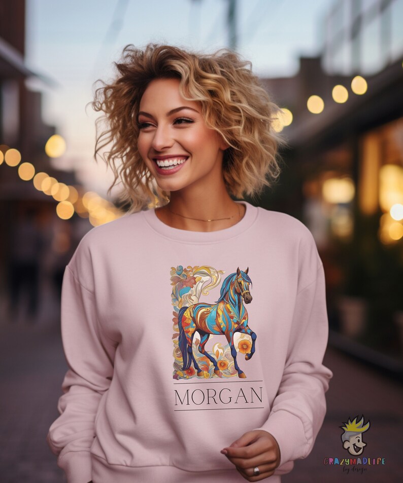 以下が含まれることがあります： カラフルな馬のデザインと「MORGAN」という名前が下に印刷されたピンク色のスウェットシャツです。