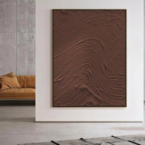 Puede incluir: Una pintura abstracta marr&oacute;n con una superficie texturizada y l&iacute;neas en espiral. La pintura est&aacute; enmarcada en un marco fino y dorado.