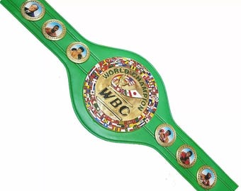 Könnte beinhalten: Grüner Lederboxgürtel mit goldenen Akzenten und einem runden Emblem mit dem Text "World Champion" und "WBC", umgeben von Flaggen verschiedener Länder.
