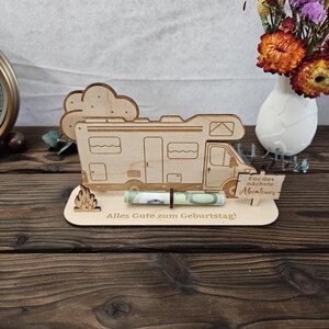 May include: A wooden campervan-shaped gift holder with a rolled-up banknote in front. The holder features a cloud and flame design, with German text reading "Alles Gute zum Geburtstag!" and "F&uuml;r das n&auml;chste Abenteuer."