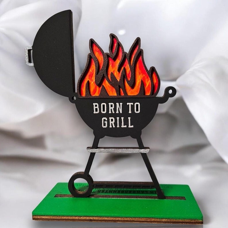 K&ouml;nnte beinhalten: Ein schwarzer und roter Grill aus Holz mit Flammenmuster und dem Text "Born to Grill".