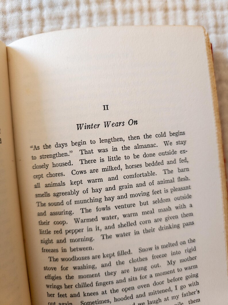 May include: Open book page with text titled "Winter Wears On." The text describes winter activities, including caring for animals and the effects of cold weather. The page has a cream-colored background with black text.