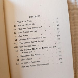 May include: Open book page with the table of contents. The text includes titles like "The New Year", "Winter Wears On", and "For All Good Things". The page numbers are listed to the right of each title. The book is open on a light-colored surface.