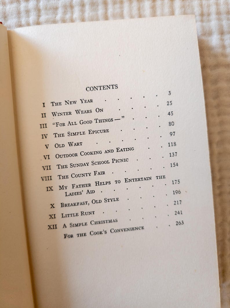 May include: Open book page with the table of contents. The text includes titles like "The New Year", "Winter Wears On", and "For All Good Things". The page numbers are listed to the right of each title. The book is open on a light-colored surface.