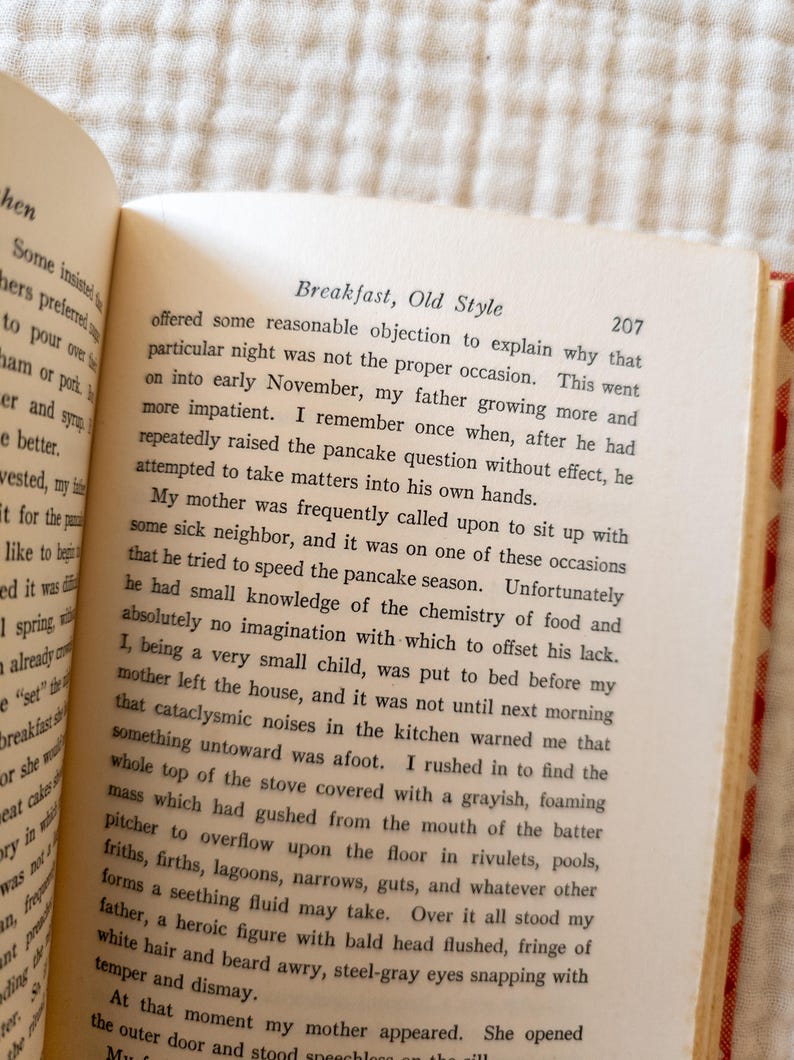 May include: Open book with text titled "Breakfast, Old Style" on a cream-colored page. The text is in black font. The book is open to page 207. The book's binding is red.