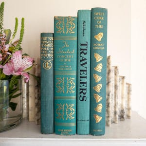 May include: Four teal-colored hardcover books standing upright, featuring gold-colored lettering and decorative motifs. The titles include The Travels of Marco Polo, The Standard Concert Guide, Travelers, and Sweet Cork of Thee, with gold bell illustrations.